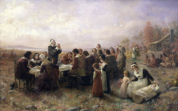 This is a painting of the First Thanksgiving at Plymouth. Pilgrims sit outside at a table praying over their meal. Native Americans sit on the ground in the background looking on. A mother rocks her baby in a wooden cradle as another young child stands beside her.